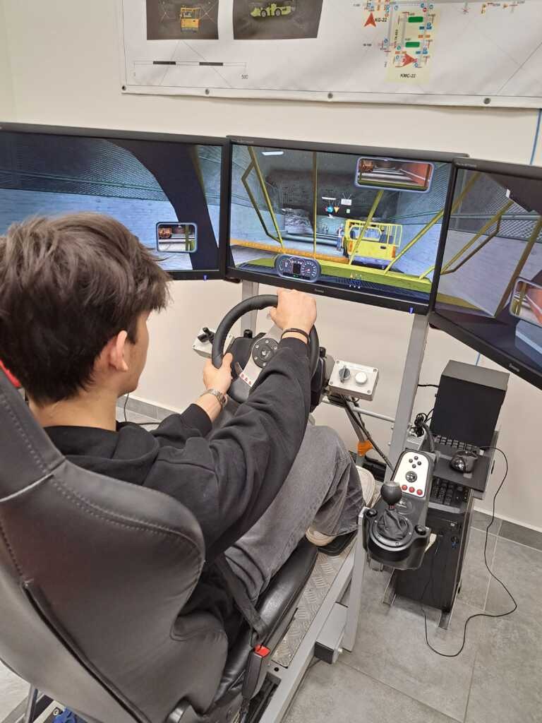 Osoba siedzi w fotelu symulatora wyścigowego, używając kierownicy i pedałów, stojąc przed trzema dużymi monitorami wyświetlającymi grę symulującą pojazd.